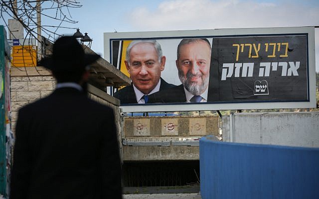 Un Juif ultra-orthodoxe devant un panneau d'affichage avec des photos du Premier ministre Benjamin Netanyahu et du chef du Shas Aryeh Deri, dans le cadre de la campagne électorale Shas, à Safed, le 10 mars 2019. (David Cohen/Flash90) Un Juif ultra-orthodoxe devant un panneau d'affichage avec des photos du Premier ministre Benjamin Netanyahu et du chef du Shas Aryeh Deri, dans le cadre de la campagne électorale Shas, à Safed, le 10 mars 2019. (David Cohen/Flash90)