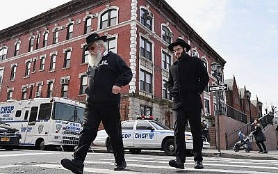 Deux Juifs orthodoxes passent à côté de véhicules de sécurité de la patrouille "Crown Heights Shmira Patrol" dans le quartier de Crown Heights, le 27 février 2019 à New York. (Crédit : Angela Weiss / AFP)