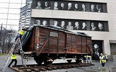 Des portraits de survivants de la Shoah affichés au musée du patrimoine juif au dessus du wagon plombé allemand, comme ceux qui étaient utilisés pour transporter les personnes à Auschwitz et dans les camps de la mort à New Yok, le 31 mars 2019 (Crédit : AP Photo/Richard Drew)