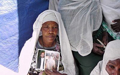 Une Ethiopienne à la synagogue d'Addis Abeba priant et tenant les photos de membres de sa famille vivant en Israël. (Crédit : Bernard Dichek/ Times of Israel)