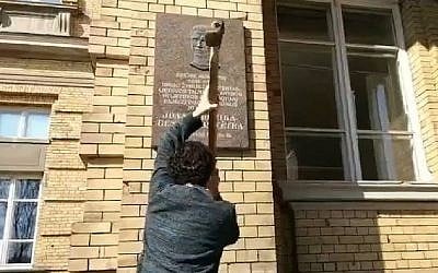 Stanislovas Tomas tente de détruire la plaque en l'honneur de Jonas Noreika à Vilnius,Lituanie,le 7 avril 2019. (Crédit : capture écran/Facebook)