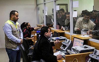 Des employés aident les Palestiniens à recevoir l'aide financière apportée par le Qatar aux familles défavorisées au bureau central de poste de Gaza City, le 26 janvier 2019 (Crédit : Mahmud Hams/AFP)