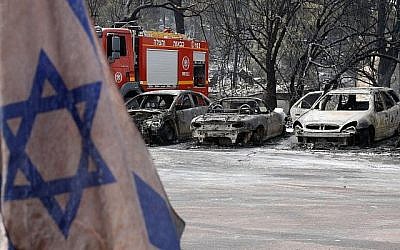 Un drapeau israélien devant des voitures très endommagées par un feu dans un contexte de chaleur extrême dans le village de Mevo Modiim dans le centre d'Israël, le 24 mai 2019 (Crédit : Jack Guez/AFP)