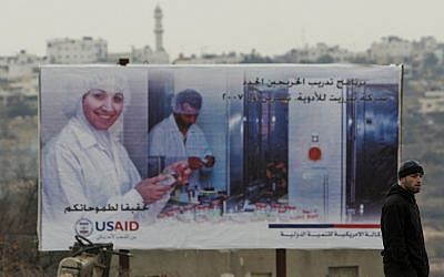 Un Palestinien passe devant un panneau de l'USAID dans la ville de Halhoul, en Cisjordanie, en 2007 (Crédit : AP Photos/Kevin Frayer) Un Palestinien passe devant un panneau de l'USAID dans la ville de Halhoul, en Cisjordanie, en 2007 (Crédit : AP Photos/Kevin Frayer)