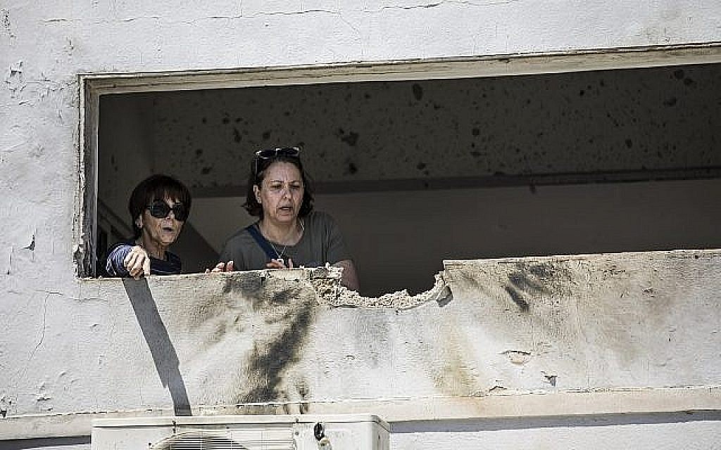 Des femmes observent les dégâts causés par une roquette tirée d'une bande de Gaza qui a touché une maison dans le sud d'Israël près de la frontière avec Gaza, samedi 4 mai 2019 (Crédit : AP / Tsafrir Abayov) Des femmes observent les dégâts causés par une roquette tirée d'une bande de Gaza qui a touché une maison dans le sud d'Israël près de la frontière avec Gaza, samedi 4 mai 2019 (Crédit : AP / Tsafrir Abayov)