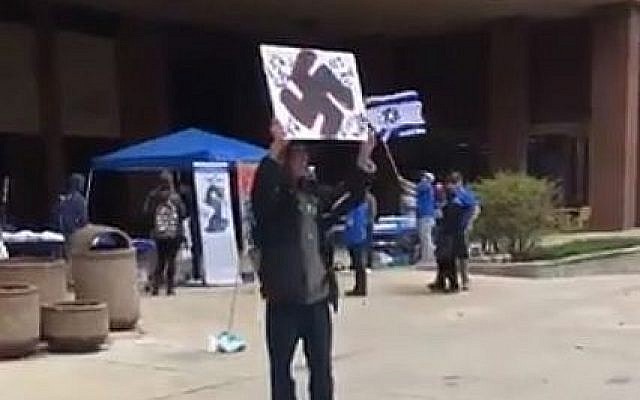 Capture d'écran d'une vidéo où l'on voit un homme muni d'un panneau avec une croix gammée lors d'une évènement pour Yom HaAtsmaout à l'université de Wisconsin-Milwaukee. (Crédit : Twitter) Capture d'écran d'une vidéo où l'on voit un homme muni d'un panneau avec une croix gammée lors d'une évènement pour Yom HaAtsmaout à l'université de Wisconsin-Milwaukee. (Crédit : Twitter)