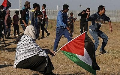 Un manifestant lance de pierres sur les soldats israéliens alors qu'une femme tient un drapeau national palestinien, lors d'une manifestation à proximité de la frontière avec Israël, à l'est de Gaza ville, le 10 mai 2019. (Said KHATIB / AFP)