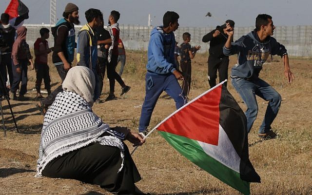 Un manifestant lance de pierres sur les soldats israéliens alors qu'une femme tient un drapeau national palestinien, lors d'une manifestation à proximité de la frontière avec Israël, à l'est de Gaza ville, le 10 mai 2019. (Said KHATIB / AFP) Un manifestant lance de pierres sur les soldats israéliens alors qu'une femme tient un drapeau national palestinien, lors d'une manifestation à proximité de la frontière avec Israël, à l'est de Gaza ville, le 10 mai 2019. (Said KHATIB / AFP)