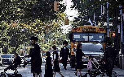Des enfants et des adultes traversent une rue devant un bus scolaire à Borough Park, un quartier de Brooklyn, New York, qui abrite de nombreux Juifs ultra-orthodoxes. (Crédit : AP/Bebeto Matthews)