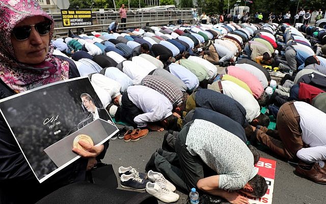 Une femme tient une photo de Mohamed Morsi lors d'une prière pour les funérailles du président, devant l'ambassade d'Ankara, le 18 juillet 2019. (Crédit : Adem ALTAN / AFP)