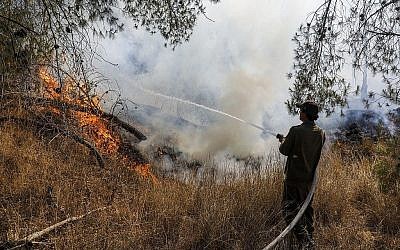 Un soldat israélien éteint un feu causé par un ballon incendiaire lancé depuis Gaza, près du kibboutz Nahal Oz, le 26 juin 2019. (Crédit : Menahem Kahana/AFP)