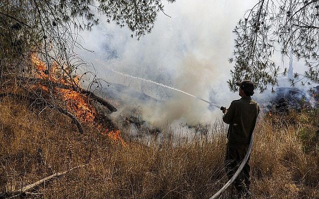 Un soldat israélien éteint un feu causé par un ballon incendiaire lancé depuis Gaza, près du kibboutz Nahal Oz, le 26 juin 2019. (Crédit : Menahem Kahana/AFP)
