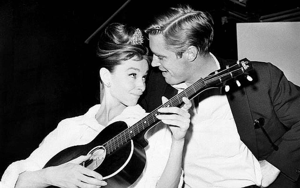 Audrey Hepburn à la guitare aux côtés de George Peppard entre deux prises sur le tournage de "Diamants sur canapé" dans un studio de Hollywood, le 7 décembre 1960 (Crédit : AP Photo)
