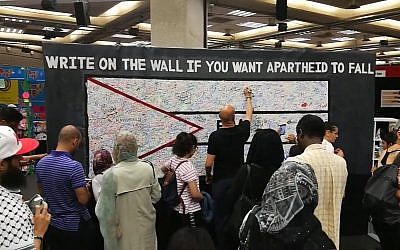 Des participants à la Palestine Expo 2017 à Lodnres écrivent sur un mur pour dénoncer "l'apartheid" israélien. Crédit : capture écran/YouTube)