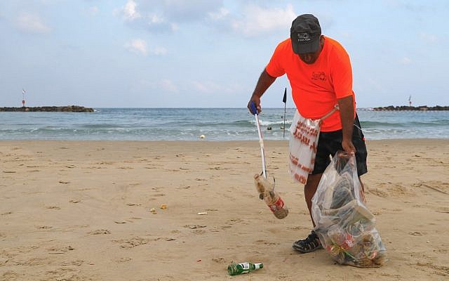 Un employé de la mairie de Tel Aviv ramasse les plastiques et autres déchets laissés sur les plages de la ville côtière israélienne, le 21 juin 2019.(Crédit : JACK GUEZ / AFP)