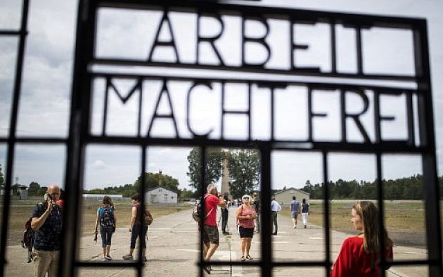Des visiteurs devant une grille de fer portant la phrase allemande "Arbeit Macht Frei" (« Le travail vous rend libre ») dans l'ancien camp de concentration de Sachsenhausen, dans l'est de l'Allemagne, le 7 août 2019. (Crédit : Odd ANDERSEN / AFP)