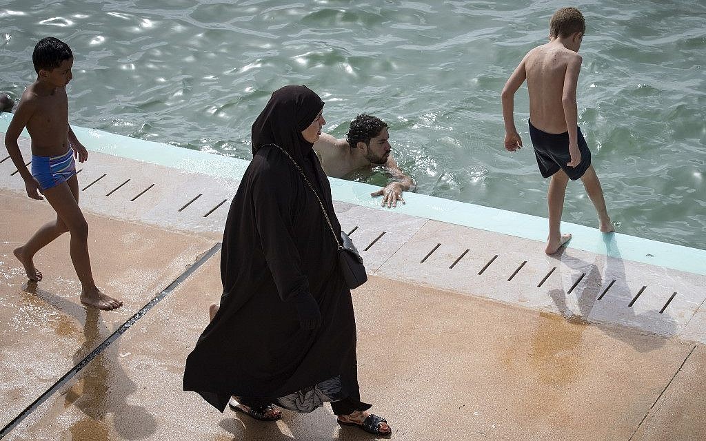 Une Marociane voile passe devant un homme à la nouvelle piscine publique de Rabat, le 7 août 2019. (Crédit ! FADEL SENNA / AFP)