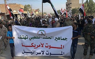 Des hommes endeuillés tiennent une affiche en arabe où l'on peut lire : "Les masses des Forces de mobilisation populaire chantent la mort à l'Amérique, mort à Israël", lors d'une procession de l'enterrement d'Abu Ali al-Dabi, un combattant des Forces de mobilisation populaire, qui a été tué dans une attaque de drone, à Baghdad, en Irak, le 26 août 2019.(AP Photo/Ali Abdul Hassan)