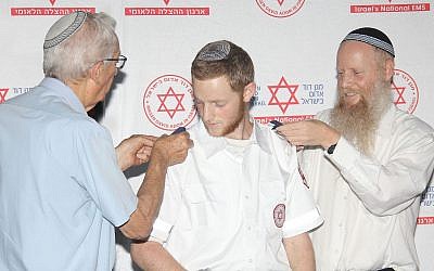 Dvir Shnerb reçoit ses galons de son père, le rabbin Eitan Shnerb et de son grand-père, Zvi Wisbert, lors de la remise de diplôme à l'issue de sa formation à Magen David Adom., le 6 septembre 2019. (Crédit : Madagascar Photography via JTA)