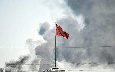 Une photo prise à Akcakale à la frontière turque avec la Syrie le 10 octobre 2019 montre le drapeau turc alors que la fumée monte de la ville syrienne de Tal Abyad après un tir de mortier qui a touché la ville d'Akcakale. (BULENT KILIC / AFP)