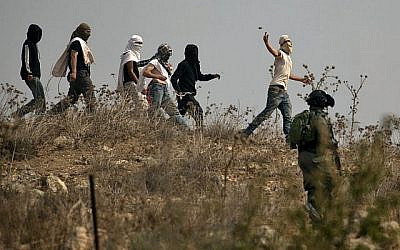 Illustration : les soldats israéliens regardent des habitants d'implantation masqués jeter des pierres à des manifestants palestiniens (non visibles sur la photo) pendant une manifestation contre la construction d'un avant-poste israélien aux abords du village de Turmusaya et de l'implantation de Shilo, au nord de Ramallah, en Cisjordanie, le 17 octobre 2019 (Crédit : JAAFAR ASHTIYEH / AFP)