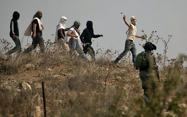Illustration : les soldats israéliens regardent des habitants d'implantation masqués jeter des pierres à des manifestants palestiniens (non visibles sur la photo) pendant une manifestation contre la construction d'un avant-poste israélien aux abords du village de Turmusaya et de l'implantation de Shilo, au nord de Ramallah, en Cisjordanie, le 17 octobre 2019 (Crédit : JAAFAR ASHTIYEH / AFP) Illustration : les soldats israéliens regardent des habitants d'implantation masqués jeter des pierres à des manifestants palestiniens (non visibles sur la photo) pendant une manifestation contre la construction d'un avant-poste israélien aux abords du village de Turmusaya et de l'implantation de Shilo, au nord de Ramallah, en Cisjordanie, le 17 octobre 2019 (Crédit : JAAFAR ASHTIYEH / AFP)