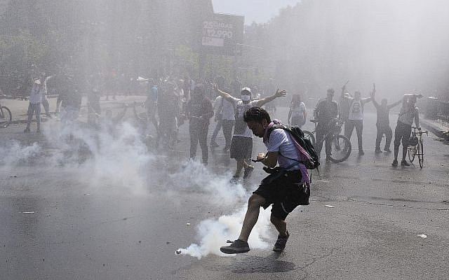 Un manifestant donne un coup de pied à une bouteille de gaz lacrymogène pendant des affrontements avec la police à Santiago, au Chili, le 20 octobre 2019 (Crédit : AP Photo/Esteban Felix)