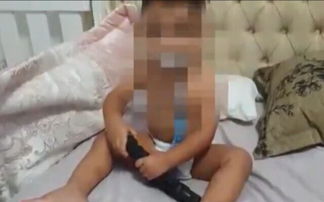 Un bébé de 18 mois filmé en train de jouer avec une arme dans son lit à Umm al-Fahm, dans le nord du pays (Capture d'écran : Kan) Un bébé de 18 mois filmé en train de jouer avec une arme dans son lit à Umm al-Fahm, dans le nord du pays (Capture d'écran : Kan)