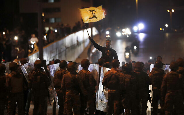 Un partisan du groupe terroriste soutenu par l'Iran, le Hezbollah, agite son drapeau alors qu'il se tient devant des soldats de l'armée libanaise après l'affrontement entre les manifestants anti-gouvernementaux et le groupe, à Beyrouth, lundi 25 novembre 2019. (Crédit : AP / Hussein Malla) Un partisan du groupe terroriste soutenu par l'Iran, le Hezbollah, agite son drapeau alors qu'il se tient devant des soldats de l'armée libanaise après l'affrontement entre les manifestants anti-gouvernementaux et le groupe, à Beyrouth, lundi 25 novembre 2019. (Crédit : AP / Hussein Malla)