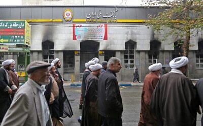 Des Iraniens passent devant une agence bancaire locale qui a été dégradée lors des manifestations contre la hausse des prix du pétrole le 20 novembre 2019 à Shahriar, à l'ouest de Téhéran. (Photo par ATTA KENARE / AFP)