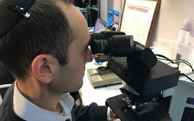 Augmentiqs a développé un appareil électro-optique qui s'intègre au sein d'un microscope déjà existant et le transforme en un objet connecté et intelligent. Le co-fondateur Gabe Siegel regarde au microscope à l'exposition HealthIL à Tel Aviv, le 27 novembre 2019. (Shoshanna Solomon/Times of Israel)
