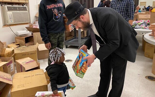 Le rabbin Moshe Schapiro montre un jouet à un enfant lors d'une initiative de charité à Jersey City, N.J., le 23 décembre 2019. (Crédit : Benny Polatseck/JTA) Le rabbin Moshe Schapiro montre un jouet à un enfant lors d'une initiative de charité à Jersey City, N.J., le 23 décembre 2019. (Crédit : Benny Polatseck/JTA)
