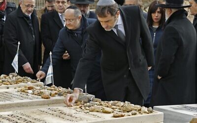 Le ministre français de l'Intérieur Christophe Castaner se rend sur les tombes des victimes de l'attentat de l'école Ozar Hatorah à Toulouse, au cimetière israélien de Givat Shaul à Jérusalem, le 23 janvier 2020. En arrière plan, Eva Sandler, qui a parti son mari et ses deux fils Aryeh et Gabriel lors de cette tuerie antisémite. (Crédit : JACK GUEZ / AFP)