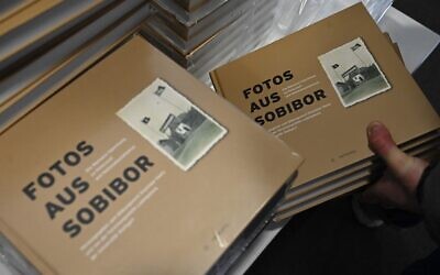 Un assistant place des livres sur une table avant une conférence de presse pour dévoiler les photos nouvellement découvertes du camp de la mort nazi de Sobibor le 28 janvier 2020 à Berlin. (Crédit :Tobias SCHWARZ / AFP)
