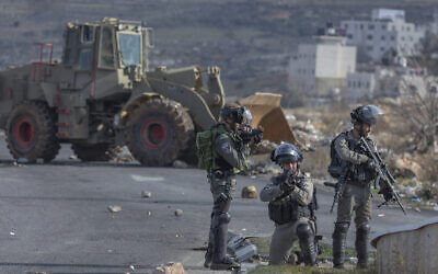 La police des frontières israélienne sécurisent une position tandis qu'un bulldozer de l'armée nettoie la route bloquée plutôt par des protestants palestiniens lors d'émeutes mineures, le 30 janvier 2020. (Crédit : AP Photo/Nasser Nasser) La police des frontières israélienne sécurisent une position tandis qu'un bulldozer de l'armée nettoie la route bloquée plutôt par des protestants palestiniens lors d'émeutes mineures, le 30 janvier 2020. (Crédit : AP Photo/Nasser Nasser)