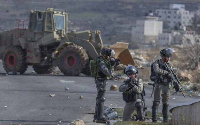 La police des frontières israélienne sécurisent une position tandis qu'un bulldozer de l'armée nettoie la route bloquée plutôt par des protestants palestiniens lors d'émeutes mineures, le 30 janvier 2020. (Crédit : AP Photo/Nasser Nasser)