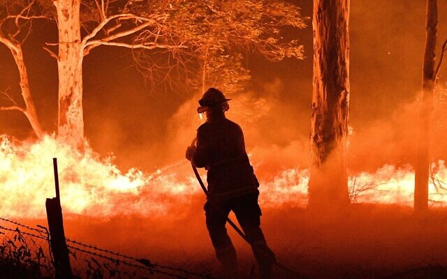 Un pompier australien arrose des arbres pour protéger des maisons avoisinantes des feux de forêts à proximité de la ville de Nowra dans l'état de South Wales, le 31 décembre 2019. Les incendies ont conduit à l'évacuation des zones populaires des touristes dans l'état. (Saeed Kahn/AFP)