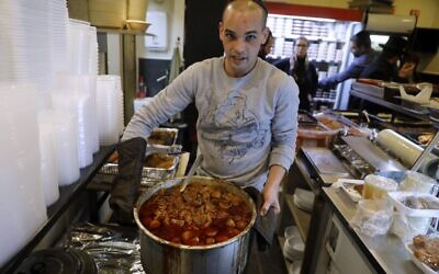 Un Israélien tient une casserole de 'Hamin, un ragoût traditionnel de la cuisine juive, au restaurant Maadaniyat Shef, à Bnei Brak le 16 janvier 2020. (Crédit : MENAHEM KAHANA / AFP)