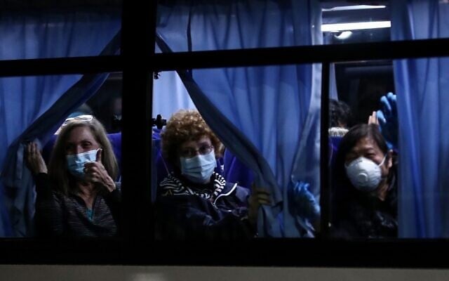 Des passagers américains saluent les journalistes en quittant le port de Yokohama,après avoir débarqué du bateau de croisière Diamond Princess placé en quarantaine pour des craintes liées au nouveau coronavirus COVID-19 à Tokyo, le 17 février 2020 (Crédit :  Behrouz MEHRI / AFP)