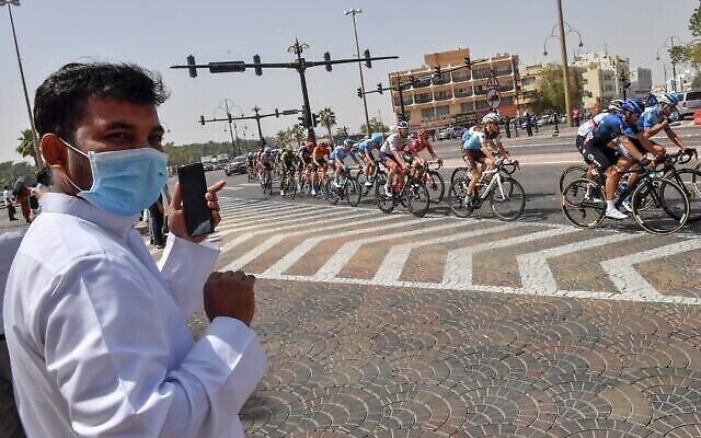 Un homme portant un masque chirurgical regarde le peloton sur la cinquième étape du Tour cycliste des Émirats, entre al-Maroum et Jebel Hafit, à Dubaï le 27 février 2020. (Crédit : Giuseppe CACACE / AFP)