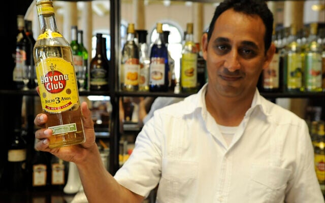 Illustration : Wilbert Wilson Rivero, un barman juif qui travaille à l'hôtel Raquel de La Havane, exhibe fièrement une bouteille de rhum Havana Club. (Larry Luxner/Times of Israel)
