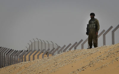 Un soldat israélien debout le long d'une section de la clôture nouvellement construite le long de la frontière avec le Sinaï en arrière-plan. (Crédit : Tsafrir Abayov/Flash 90)