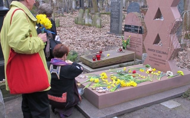 Des visiteurs placent des jonquilles sur la tombe de Marek Edelman, commandant du soulèvement du ghetto de Varsovie, dans le cimetière juif de Varsovie. (Ruth Ellen Gruber / JTA)