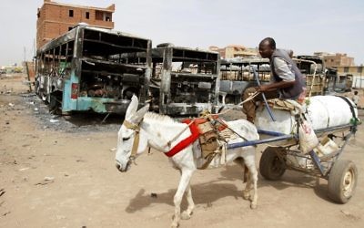 Un homme sur une charrette tirée par un âne passe devant des bus incendiés à la suite d'émeutes et de troubles à Khartoum, au Soudan, le jeudi 26 septembre 2013. (Crédit : AP Photo/Abd Raouf)
