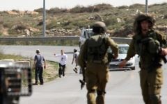 Des soldats israéliens près d'habitants des implantations qui auraient attaqué vendredi la voiture d'un photographe, à côté de l'implantation de Beit El en Cisjordanie (Crédit : AFP)