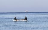 Des pêcheurs palestiniens assis dans leur barque à proximité du rivage de Rafah, au sud de Gaza ; un bateau de police israélien apparaît au loin, le 26 mars 2014. (Crédit : Said Khatib/AFP)