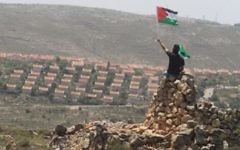 Un homme agite un drapeau palestinien devant l'implantation d'Ofra en Cisjordanie, près de Ramallah. Illustration. (Crédit : Issam Rimawi/Flash90)