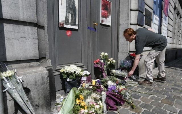 Un homme dépose une gerbe de fleurs devant la porte du musée juif de Bruxelles (Crédit : AFP)