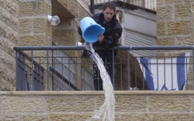 Un homme jetant de l'eau d'un balcon à Jérusalem (Crédit : Uri Lenz/Flash 90) Un homme jetant de l'eau d'un balcon à Jérusalem (Crédit : Uri Lenz/Flash 90)