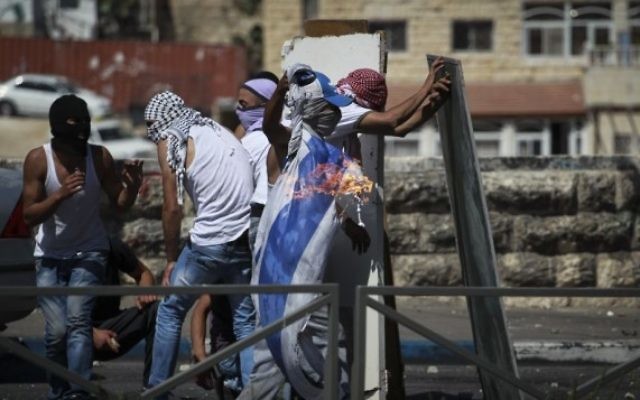 Des activistes palestiniens jettent des pierres et brûlent un drapeau d'Israël à Shuafat (Crédit : Hadas Parush/Flash 90)